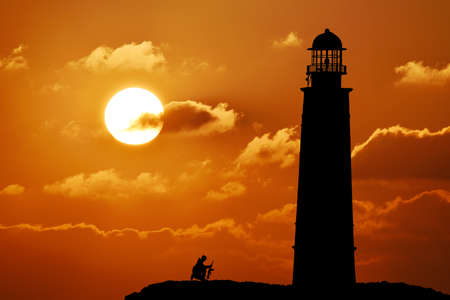 Silhouette of lighthouse at sunset. Big orange sun and cloudsの写真素材