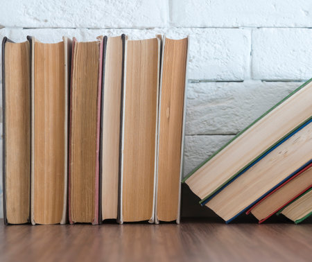 A stack of hardcover books on a wooden table against a white brick wall. copyspace.の写真素材