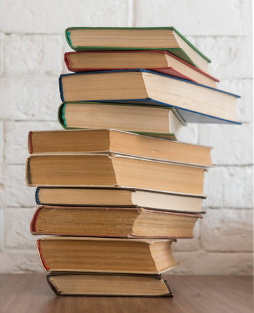 A stack of hardcover books on a wooden table against a white brick wall. copyspace.の写真素材