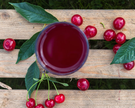 a glass with cherry juice and cherry berries with leaves on a wooden box background. flat lay and copy space.の写真素材