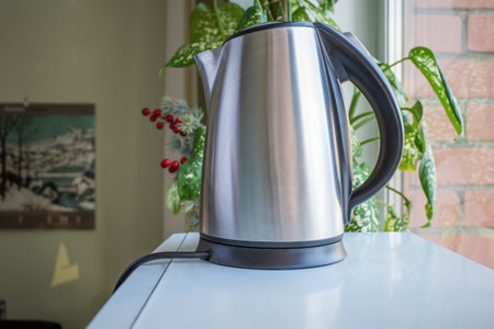 a metal silver electric kettle stands near the window in an office space against the background of a...