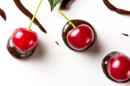 cherry berries with tails are immersed in chocolate paste on a white background. flat lay and copy space.の写真素材