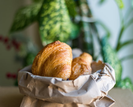 croissants in a paper bag on the background of house plants inside the office. close-up