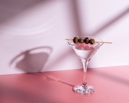 a martini glass with olives on a pink background and the shadows. copyspace.の写真素材