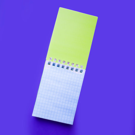 a notebook with a yellow cover on a blue background. clean sheets in a cage. flat lay and copy space.の写真素材