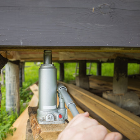 hydraulic jack for moving and raising the level of the house to a higher one. Wooden floor in the background of the house.の写真素材