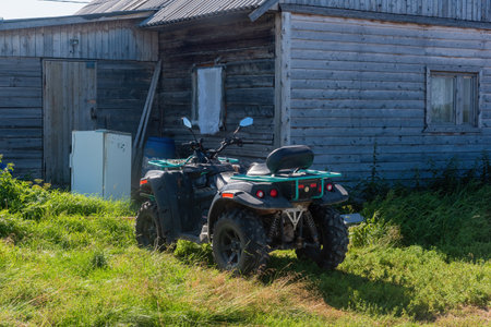 quad bike ATV is standing in the grass next to an abandoned wooden house. the concept of travel and tourism.の写真素材