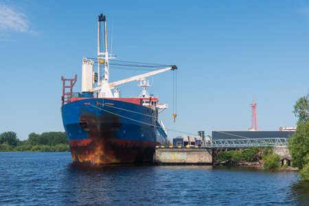 a marine vessel carries out loading at the pier. against the background of blue sky and green coastの写真素材