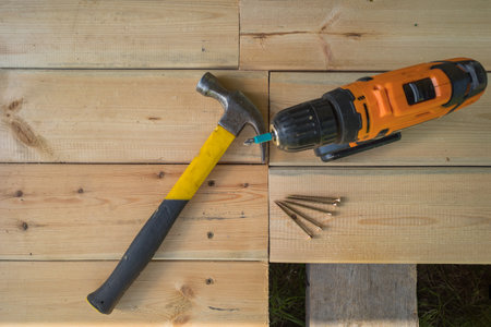 a cordless screwdriver and a bunch of screws and a hammer next to it on the background of wooden boards. copy space.の写真素材