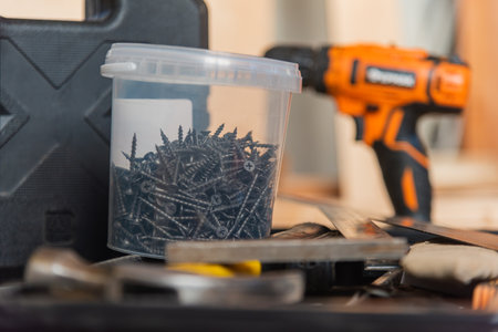 plastic jar with black screws on the background of a cordless screwdriver, his case and a hammer....