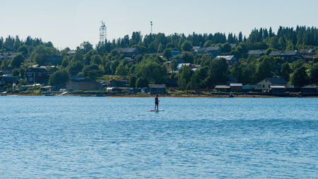 a man sails on a sap board along the bay against the background of the fishing village of Umba in...