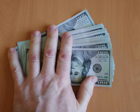 The man's hand holds out hundred dollar bills on the table. closeup and copy space.