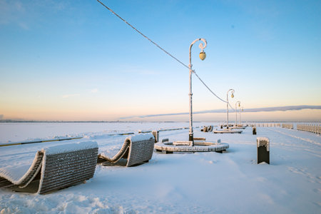 snow-covered benches on the embankment against the background of the frozen Severnaya Dvina River in Arkhangelskの写真素材