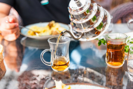In an oriental restaurant tea is poured from a shiny metal teapot with a narrow spout into a special glass cup.の写真素材