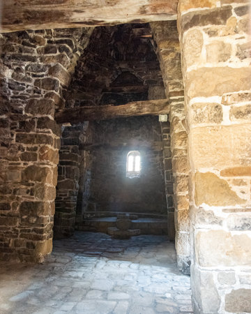 Internal stone vaults in an ancient Christian temple against the background of a small window in the wall through which sunlight can be seenの写真素材