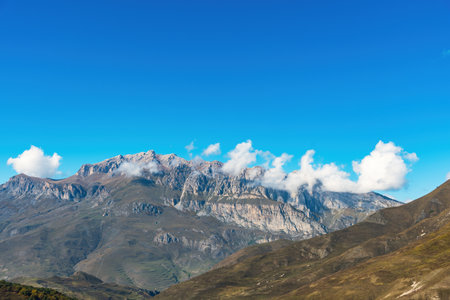 a view of the mountain tops shrouded in clouds against the blue sky. natural light