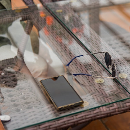 smartphone and sunglasses on the glass of a table in a cafeの写真素材
