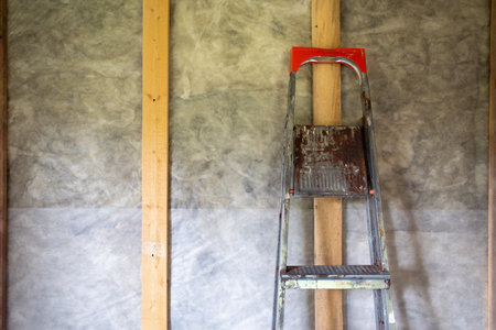 portable old iron ladder leaning against an insulated wall of a frame house inside the room. construction and renovationの写真素材