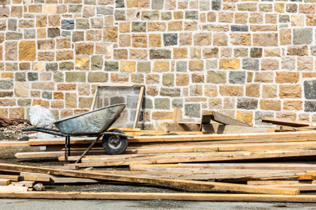 Workspace: Construction materials and a wheelbarrow in front of a stone wall at a construction site. copy spaceの写真素材