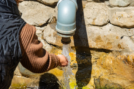 Close-up of a woman taking spring water flowing from a pipe in her palm outdoor against the background of a stone wall. natural lightの写真素材