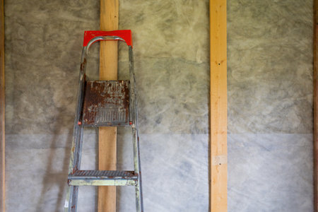 rusty metal ladder leaning against a wooden beam with a red top step.の写真素材