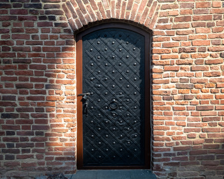 Black, ornate metal door surrounded by brick. Black Riveted Doorの写真素材
