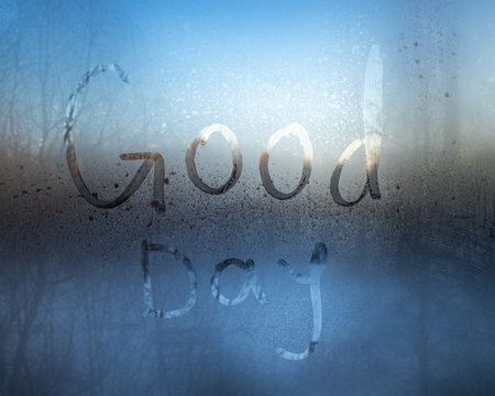 words Good Day are written in condensation on a foggy window, with a soft, blurred background of trees and sky.の写真素材