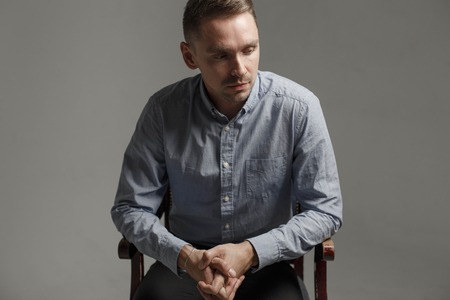 young man thinking about something sitting in chairの写真素材