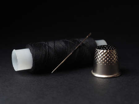 thimble and needle with thread on black background