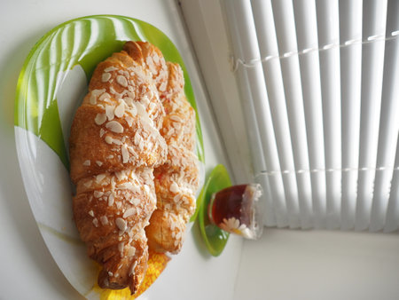 Croissants with honey and almonds on a green plate on the windowsillの写真素材