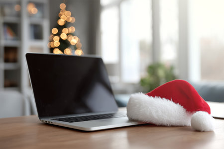 Laptop on table with Christmas hat and festive decor in backgroundの素材