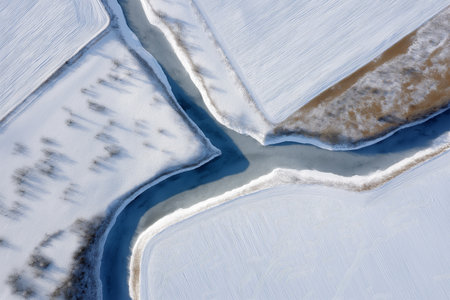 Frozen river merging with snowy fields in winter landscapeの素材