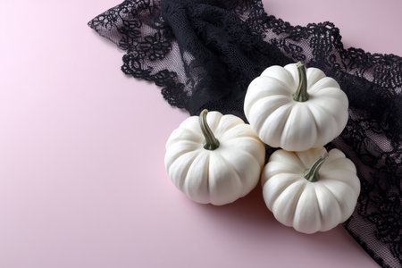 White pumpkins arranged on black lace against pink backgroundの素材