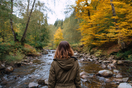 Woman standing by stream surrounded by autumn foliageの素材