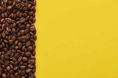 Roasted coffee beans on yellow background with copy space. Close up top view. High quality photo