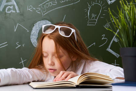 Girl schoolgirl knowledge, girl at the table wearing glasses at the blackboard.