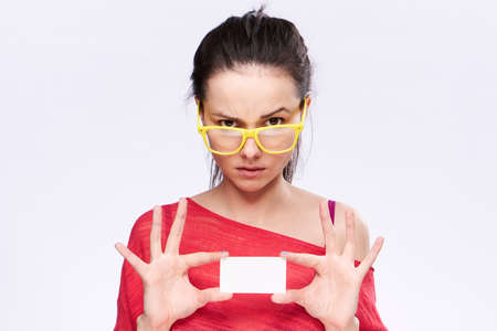 Woman in glasses holding a business card on a light background.の写真素材