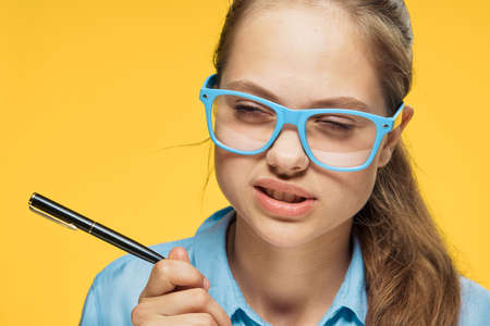Woman in glasses holds a pen on a yellow background portrait.の写真素材