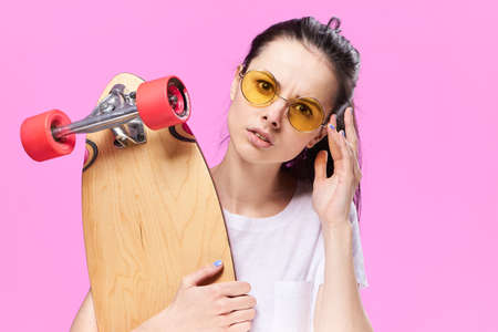 Woman with glasses, with a skateboard on a pink background.の写真素材