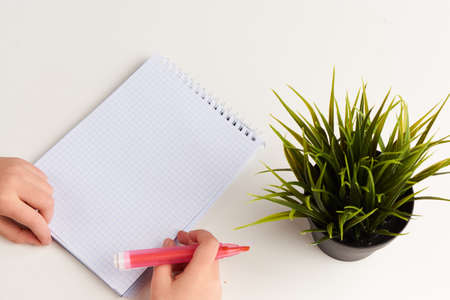 On the table is a flower, a notebook is lying, the girl is holding a felt-tip pen.の写真素材