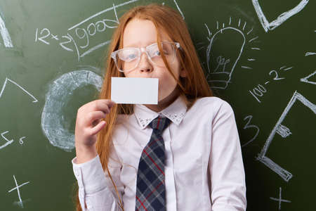 Schoolgirl with glasses piece of paper on the background of school board.の写真素材