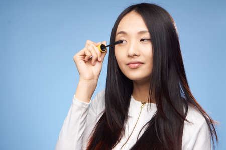 Woman with mascara, a woman paints her mascara with ink on a blue background.の写真素材