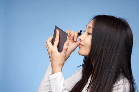 Woman paints eyelashes with mascara, woman looks in mirror on blue background.の写真素材