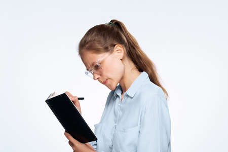 Business woman with glasses writes in a notebook with a pen on a light background.の写真素材