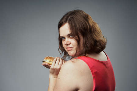 Woman with a hamburger, healthy lifestyle on a gray background.の写真素材