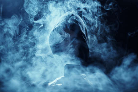 Programmer in a smoggy background, a hacker with a phone on a dark background.の写真素材