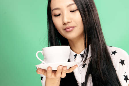 Woman holding a mug with a saucer, woman looking at a mug on a green background.の写真素材