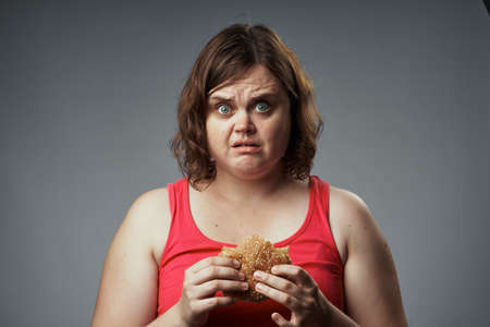 Surprised woman holding a hamburger on a gray background.の写真素材