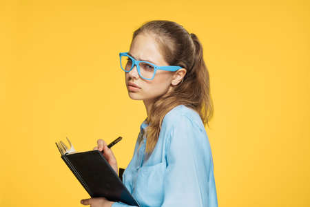 Female student with glasses thinks a woman is holding a notebook with a pen on a yellow background.の写真素材