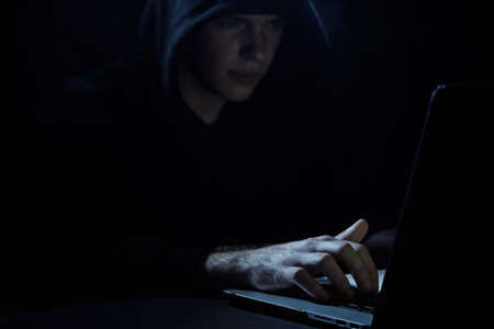 Hacker hacks computer networks on a dark background, a programmer in a hood.
